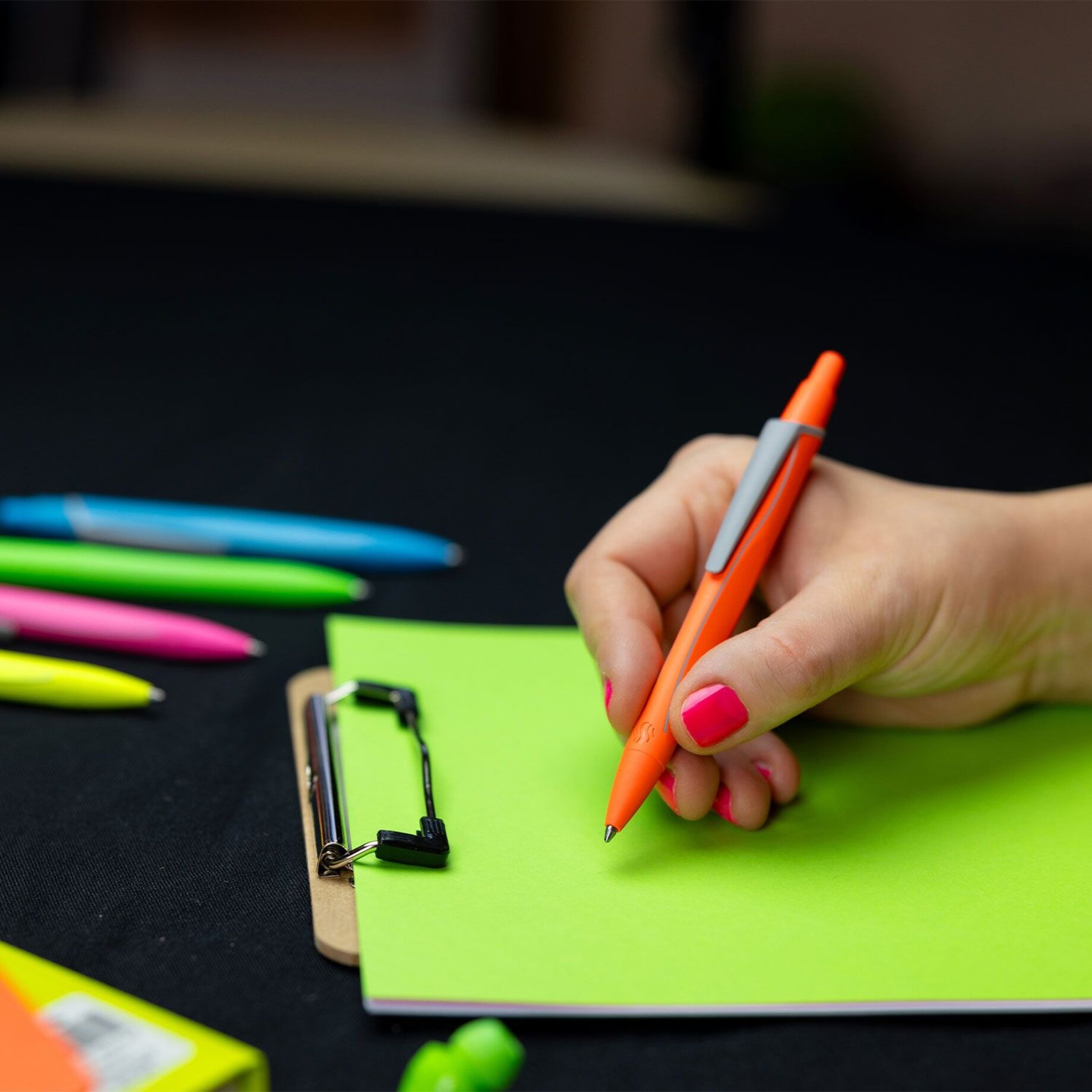 neon-orange pen, orange ballpoint, notebook, green paper, clipboard